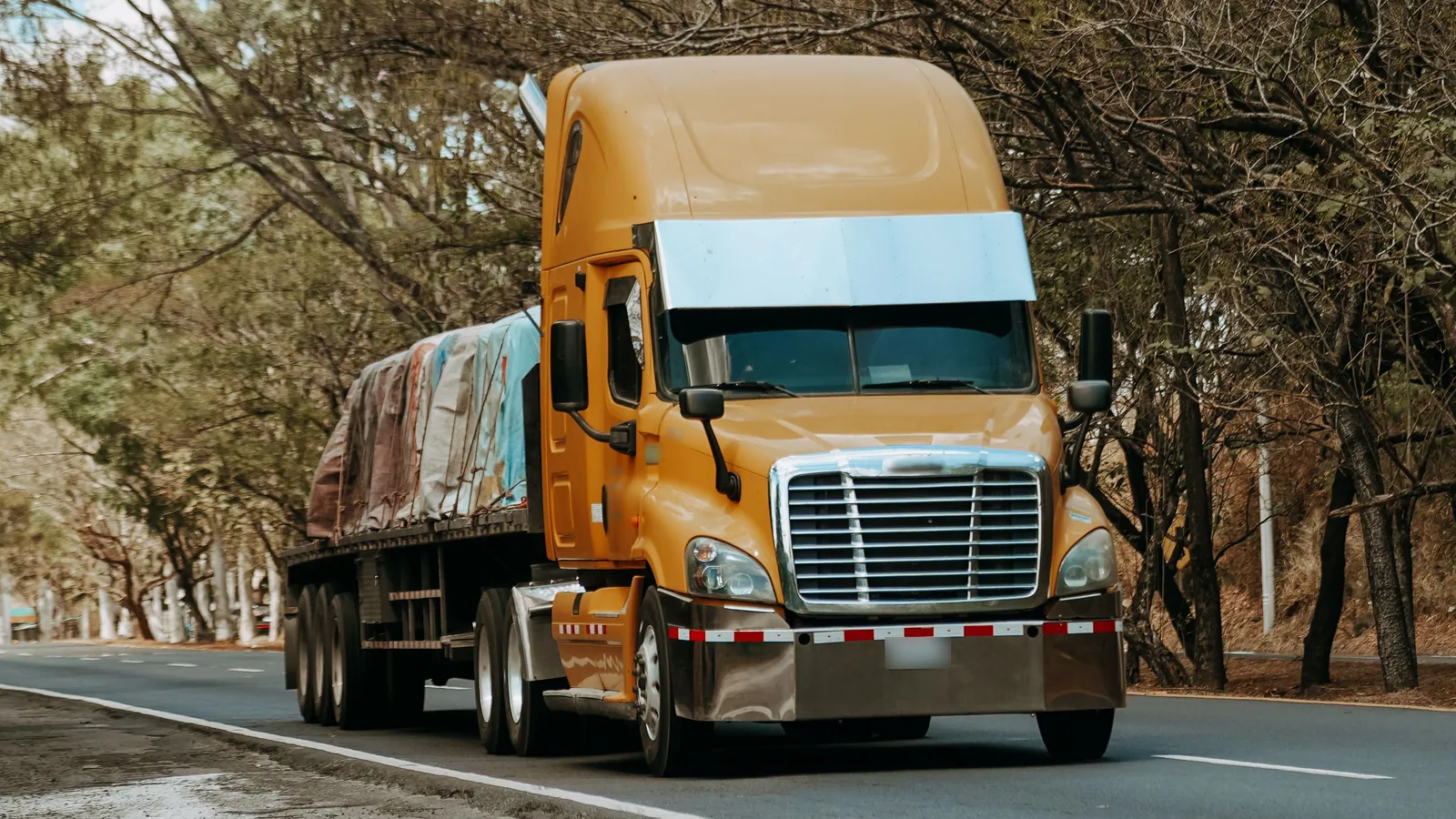 Cabezal amarillo arrastrando una plataforma cargada por una carretera arbolada